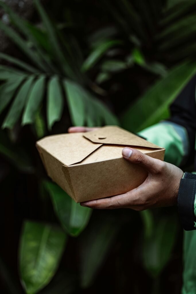 Close-up of hands holding an eco-friendly meal box against lush green leaves.