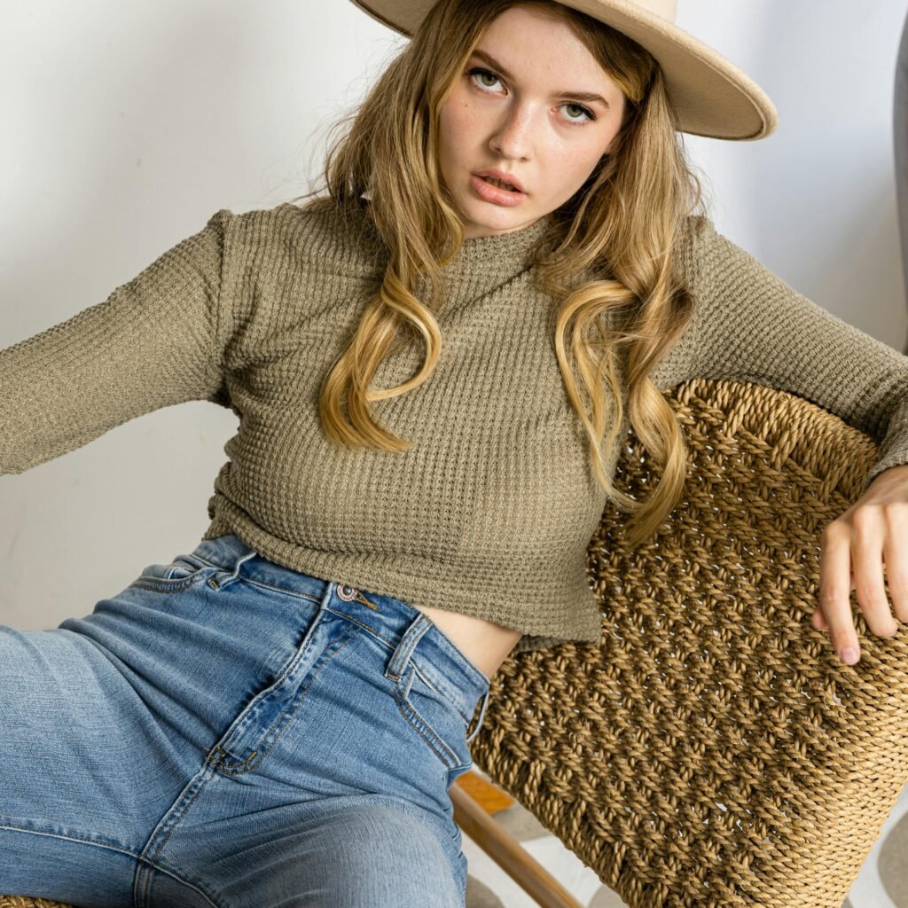 Stylish young woman wearing hat and casual attire poses indoors, showcasing a relaxed and fashionable vibe.