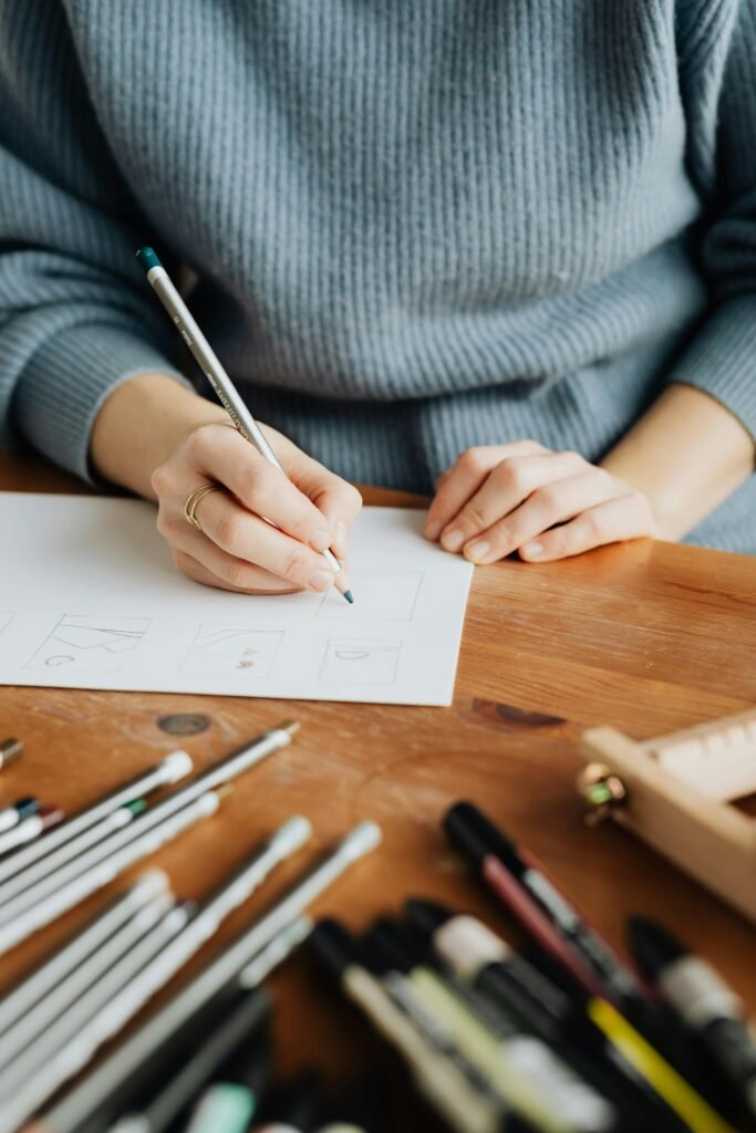 A woman sketching designs at a wooden desk with various drawing tools.
