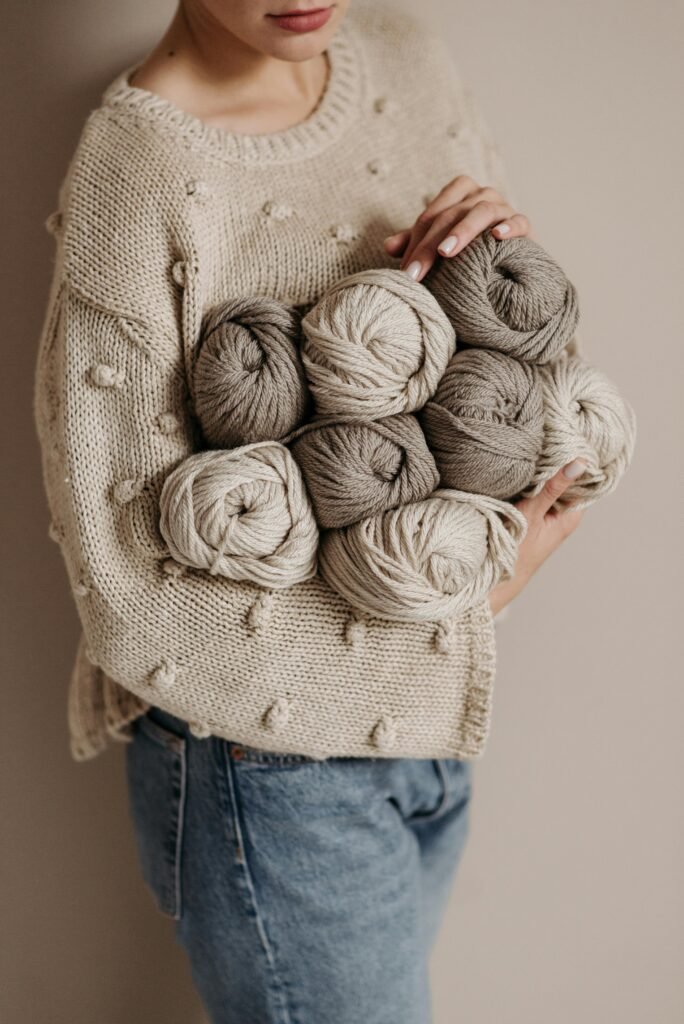Stylish woman in a knitted sweater holding yarn balls for crafting projects.