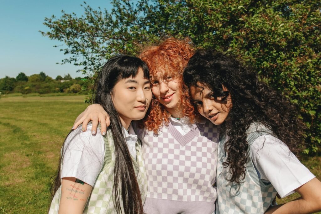 Three young women embracing and smiling outdoors on a sunny day.